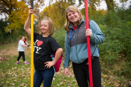 A girl and a teacher smile and hold rakes in the classroom garden.
