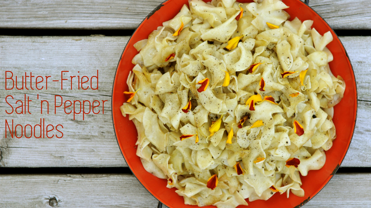 Butter fried salt and pepper egg noodles in an orange bowl with flower garnishes. Click for recipe.