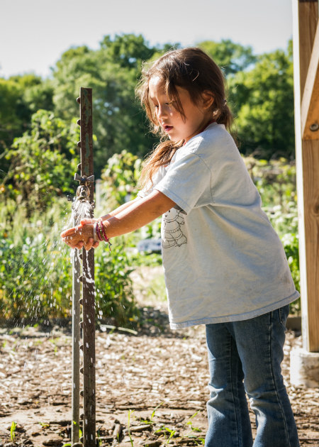 Girl washing hands in the garden spigot. Photo by Nick Bernard Photography.