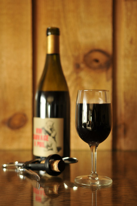 A glass of red wine in the foreground with a bottle and corkscrew in the background.