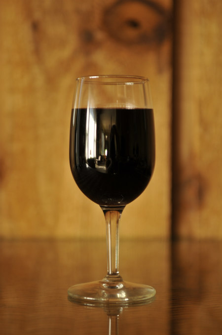 A glass of natural red wine against a wall of knotty wood.